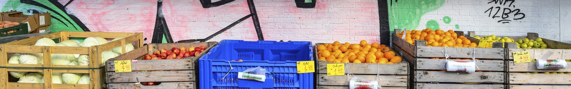 Unterschiedliches Obst in großen Boxen vor einer Wand, die mit Graffiti besprüht ist.
