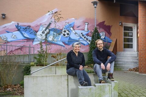 Haleh Soleymani und Guido Hanslik sitzen draußen vor einem Gebäude.