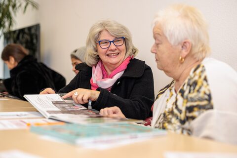 Zwei Frauen sitzen an einem Tisch und lesen ein Buch.