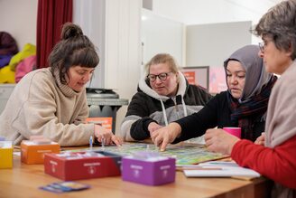 Vier Frauen sitzen an einem Tisch und spielen ein Brettspiel.