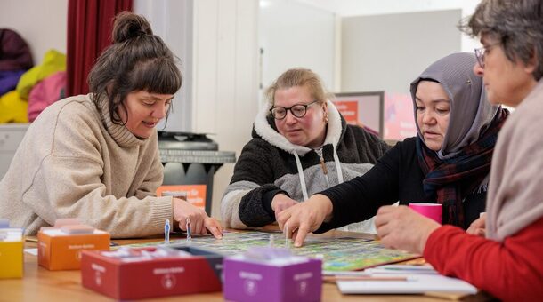 Vier Frauen sitzen an einem Tisch und spielen ein Brettspiel.