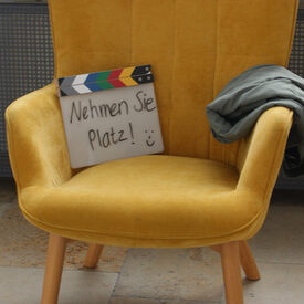 Gelber Sessel mit Schild "Nehmen Sie Platz"