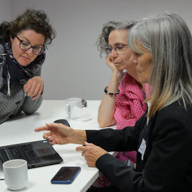 Drei Teilnehmerinnen schauen gemeinsam auf ein Laptop