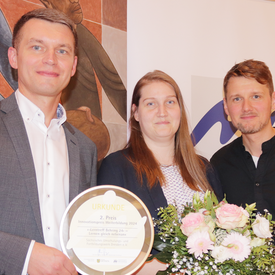 Von links nach rechts: Gino Schneider (Vorstand Sächsisches Umschulungs- und Fortbildungswerk Dresden e. V.), Stefanie Elies (VHS Dresden) und Georg Mühlberg (Leitung Lerntreff „Behring24“). Sie nehmen die Urkunde für den 2. Platz entgegen und lächeln in die Kamera.