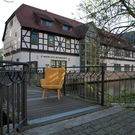 Gelber Stuhl steht auf einer Brücke vor einem Fachwerkhaus.